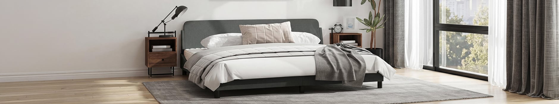Een overzichtsopname van een moderne slaapkamer met een donkergrijs bedframe, wit beddengoed en een beige kussen met rasterpatroon. De kamer heeft twee houten nachtkastjes met lampen, een hoge plant in pot en grote ramen met grijze en witte gordijnen die uitkijken op groene bomen.