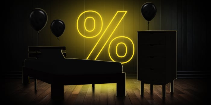 Zwart bed en ladekast met zwarte ballonnen voor een felgeel procentteken op een donkere houten vloer.